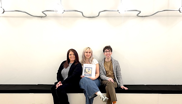Three people sit close together on an indoor bench, smiling.